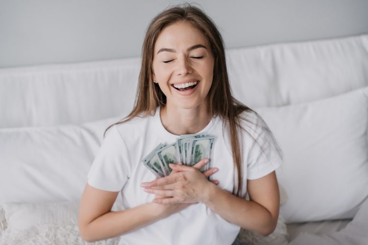 Happy young woman clutches money to her chest after saving money by bundling insurance - cheap car insurance.