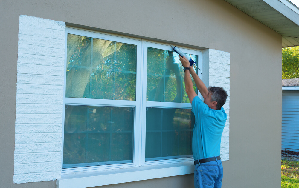 Homeowner caulks the exterior of the home windows as part of spring cleaning maintenance and to prevent leaks.