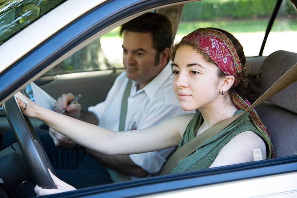A young student driver takes a driving test with the instructor in the passenger seat.
