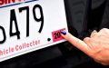 Hand pointing to a registration sticker on a car license plate, a key step when registering your car in a new state.