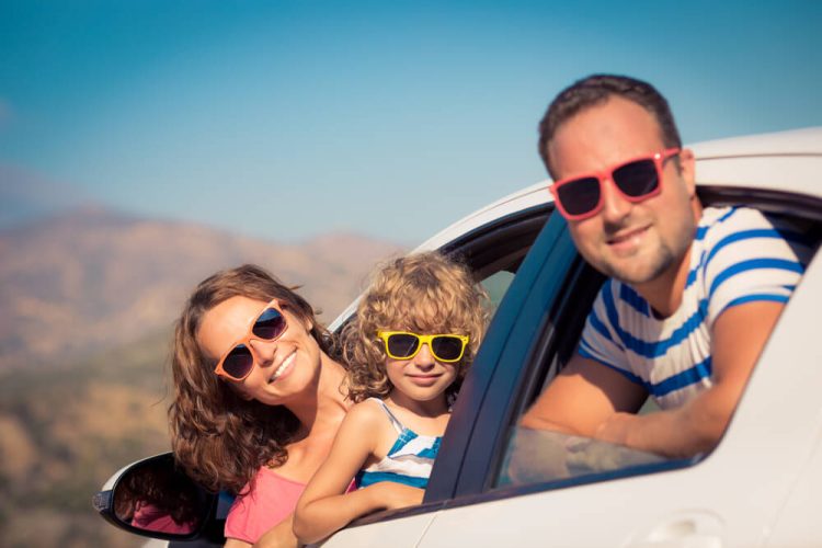 Family peeking out of their car window wearing their sunglasses, smiling for a summer trip - Freeway, cheap auto insurance.