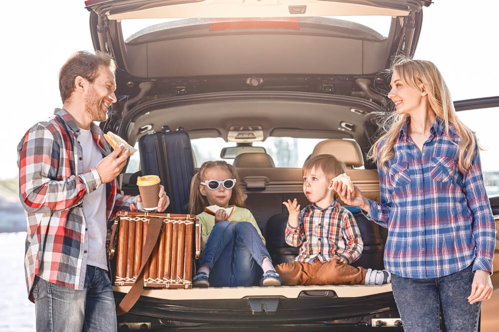 Family in the back of their vehicle enjoying a meal in the middle of a summer trip.