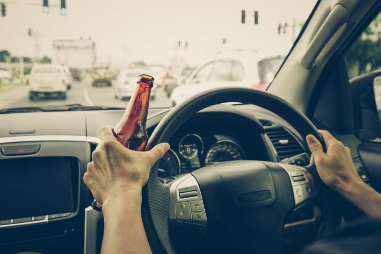 Someone driving a car with a bottle of beer in their hand.
