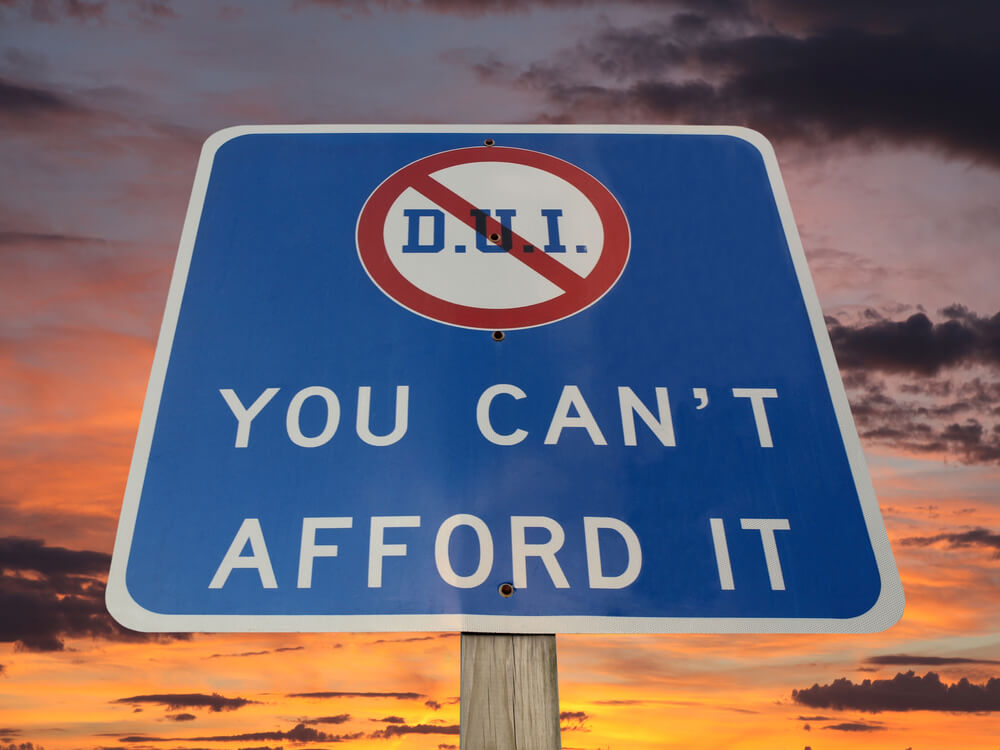 A sign against a sunset: DUI with a red mark through it and the words you can't afford it.