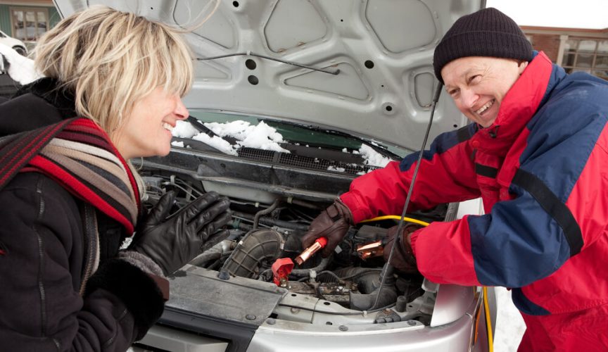 A roadside assistance technician helps jump start a woman's stranded car - cheap roadside assistance.