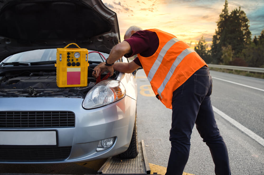A roadside assistance technician uses a battery tester to check the battery voltage on a stranded car - cheap roadside assistance.