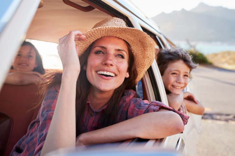 Mother looks out the front window of the car while two children are in the back seat.