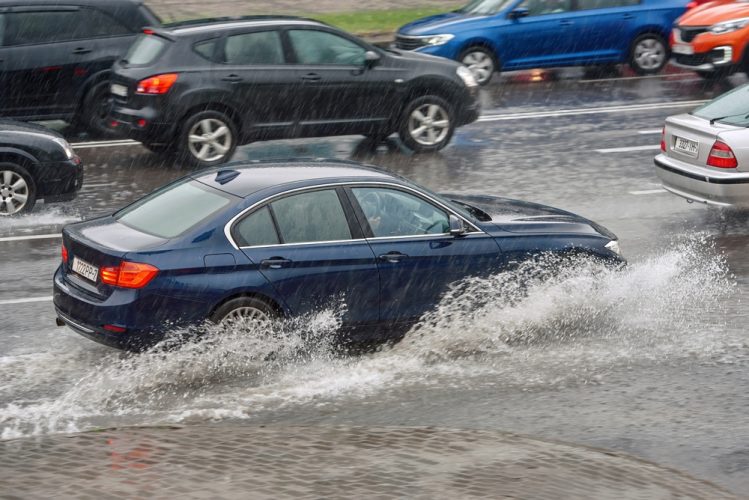 A car drives through a flooded street - cheap car insurance.