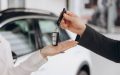 Man's hand passes car keys over to woman's hand with car in background - cheap car insurance.