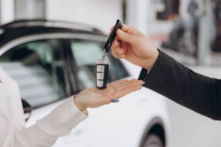 Man's hand passes car keys over to woman's hand with car in background - cheap car insurance.
