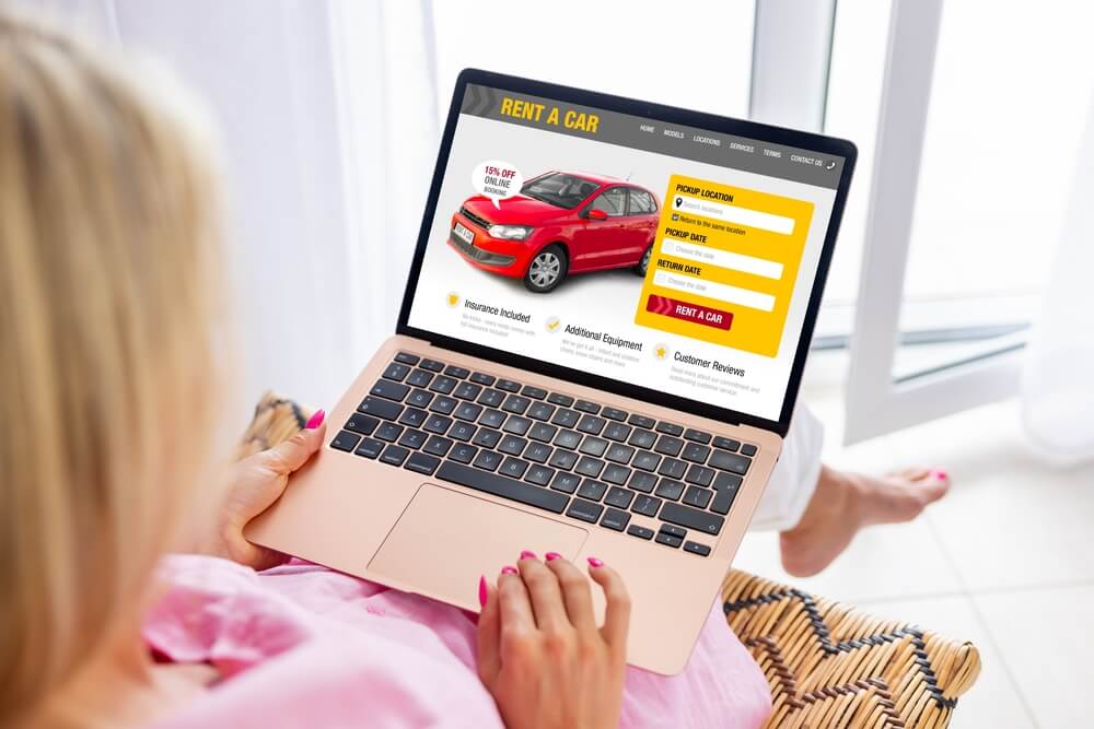 Woman with pink shirt seen from over her shoulder looking at laptop to rent a car - cheap car insurance.