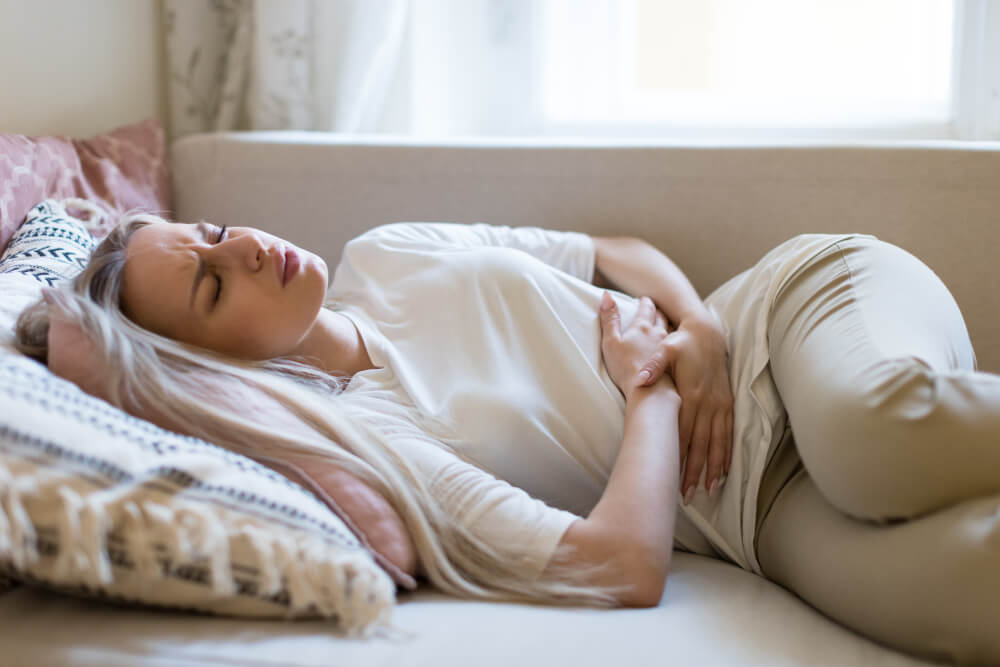 Woman lying on couch with stressed expression, in pain, holding her stomach.