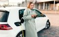 Lady stands next to her electric car while it charges at a station - cheap car insurance.