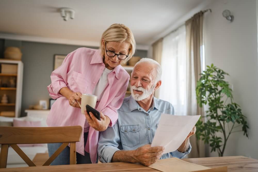 Senior couple read a document and use cellphone together to compare insurance from Freeway and Geico.