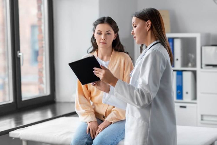 Medicine, healthcare and people concept - female doctor with tablet pc computer talking to woman patient at hospital, help finding cheap health insurance in California.