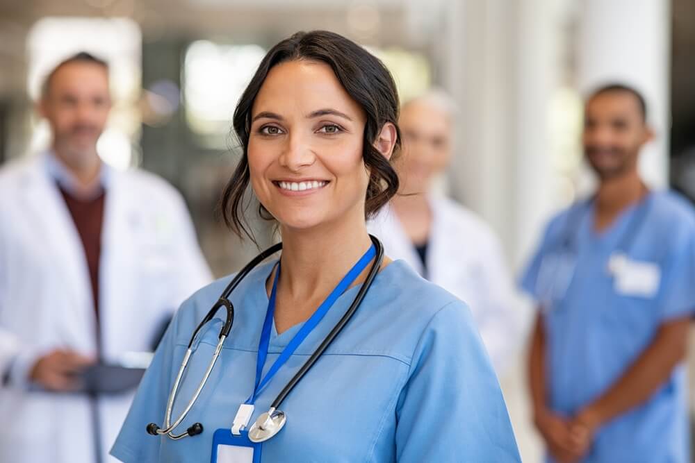 Portrait of happy young nurse in uniform with healthcare team in background. Successful team of doctor and nurses smiling, health insurance in California.