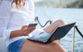 Woman works on her laptop looking for boat insurance for first-time boat owners while sitting on her boat in the water.