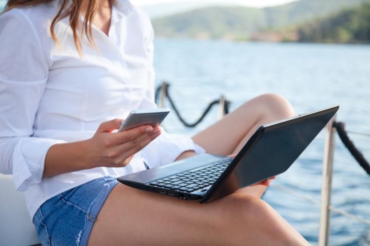 Woman works on her laptop looking for boat insurance for first-time boat owners while sitting on her boat in the water.