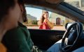 Mom and dad in their car watching their daughter on her first day of school in front of her school after getting through the back-to-school traffic.