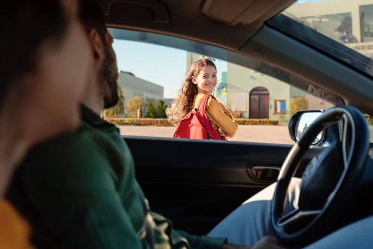 Mom and dad in their car watching their daughter on her first day of school in front of her school after getting through the back-to-school traffic.
