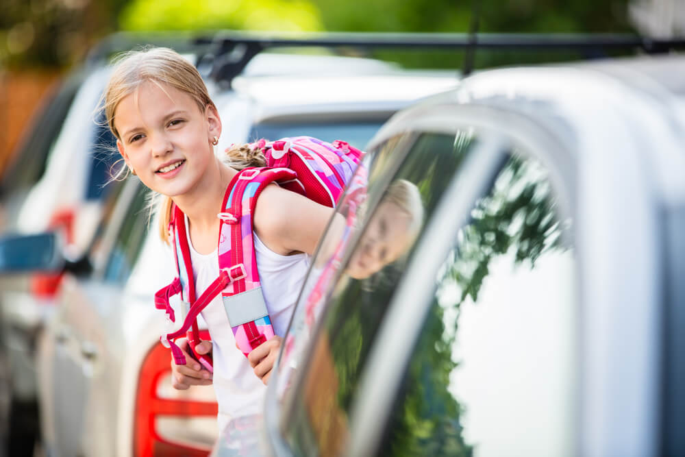 Schoolgirl with her backpack between vehicles in back-to-school traffic.
