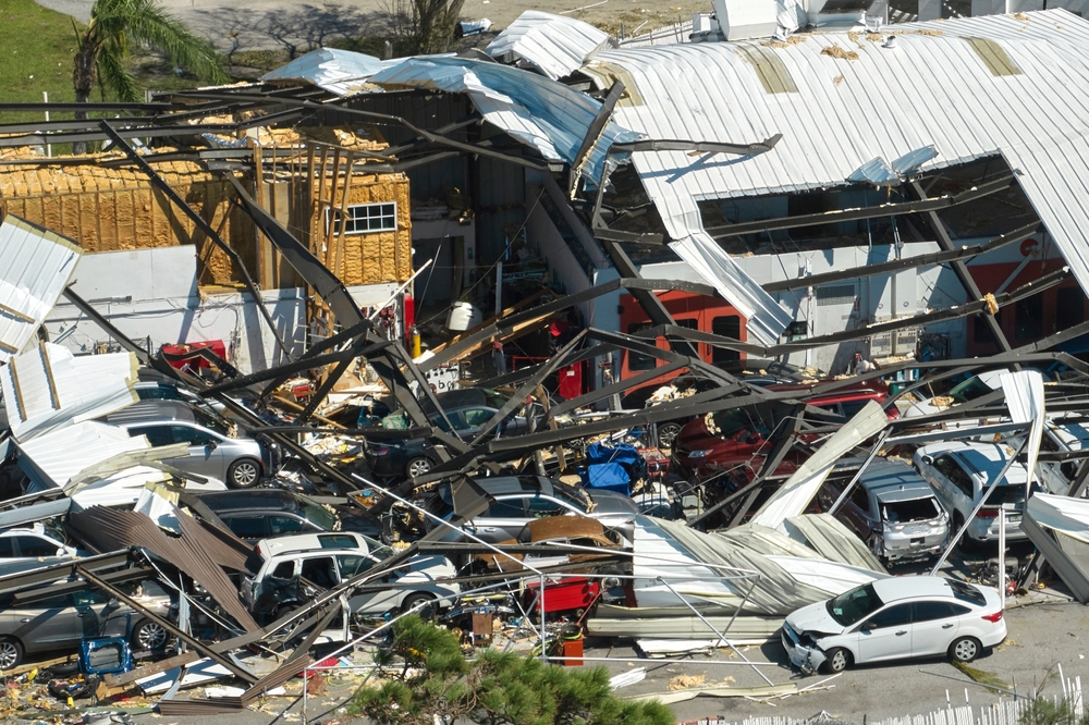 Hurricane Ian destroyed industrial building with damaged cars under ruins in Florida, causing auto insurance rate increase 2025. Natural disaster and its consequences, auto insurance rates increase.