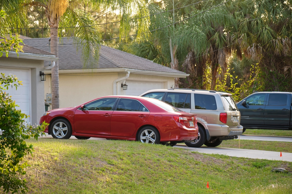 Vehicles parked in front of wide garage double door on paved driveway of typical contemporary American home, concept of bundling auto and home insurance to help with auto insurance rate increase 2025.