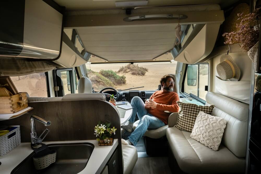 Adult traveler man sit down inside modern cozy mobile home camper van looking nature outside. Travel and van life lifestyle with the best van life insurance.