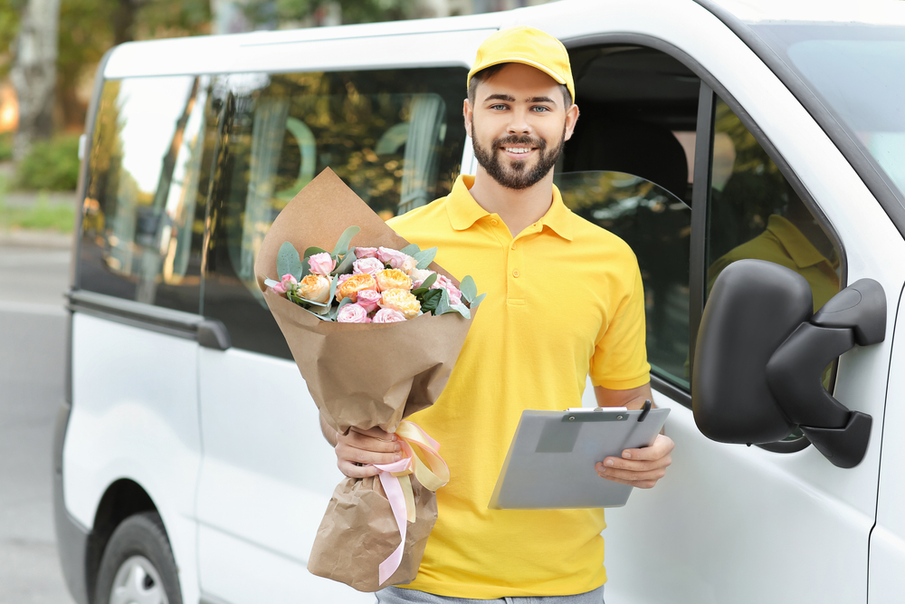 Delivery man with bouquet of beautiful flowers near delivery van protected with commercial auto insurance.