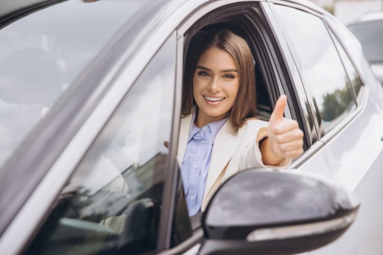 Young woman smiling and giving thumbs up inside her car after getting affordable car insurance in big cities