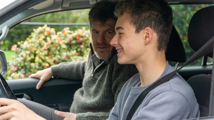 A father teaches his teenage son how to drive.