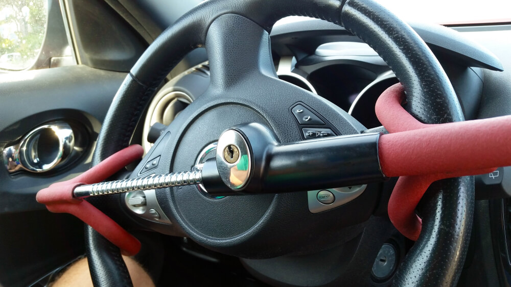 Steering wheel secured with a visible metal lock bar inside a parked car, one of the Best Car Theft Deterrent Devices to discourage theft.