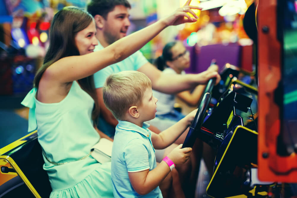 Family mother, father, teen girl with glasses and little boy driving car arcade in game machine while waiting for the races to start at Daytona.
