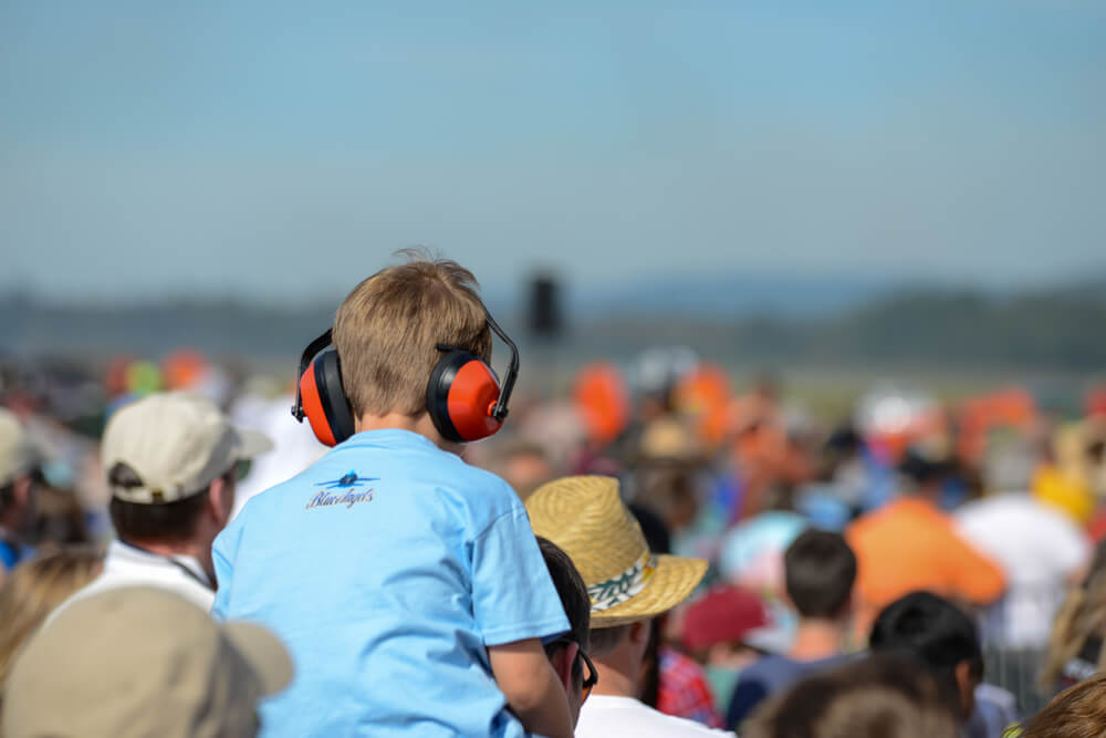 A kid is wearing earmuffs as a hearing protection at the race.