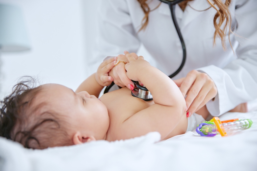 Doctor using a stethoscope to examine a newborn baby during a checkup, highlighting the importance of newborn health insurance.