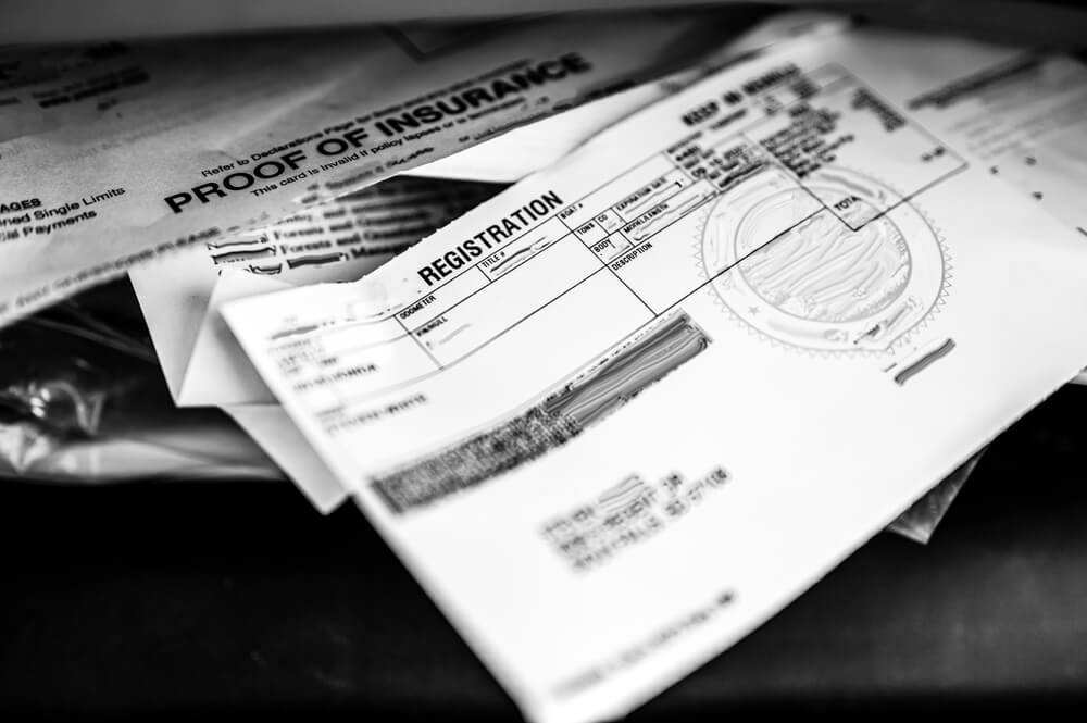 Close-up of car paperwork including registration and proof of insurance documents stacked together, useful when registering your car in a new state.