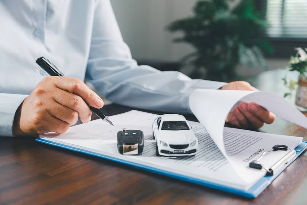 Person reviewing car insurance paperwork with keys on the desk, representing proof of car insurance documentation.