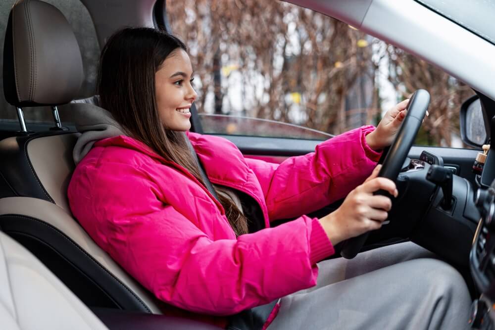 Young woman confidently driving a car, representing a new driver gaining experience with student driver stickers.