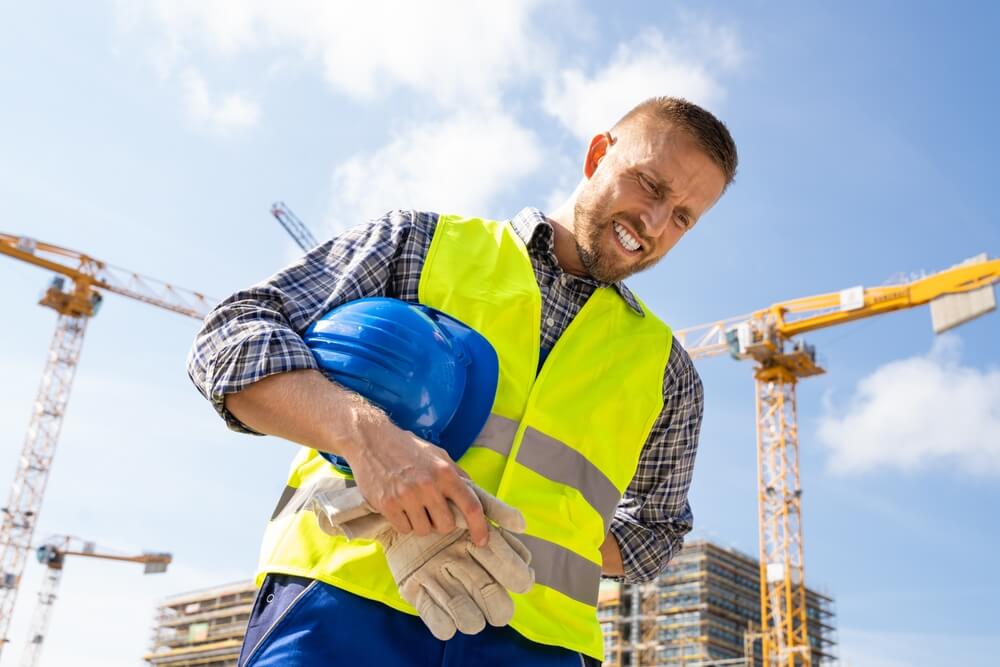Construction worker holding his side in pain at a job site, illustrating workers’ comp and general liability insurance needs.