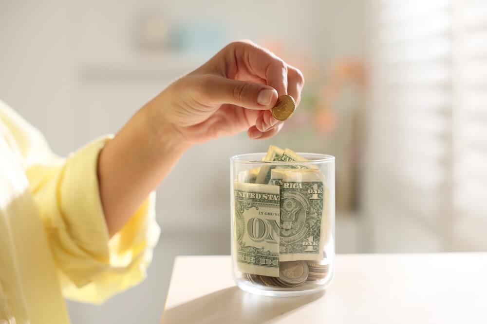 Hand placing coins into a savings jar, symbolizing budgeting and planning to compare car insurance quotes for better rates.