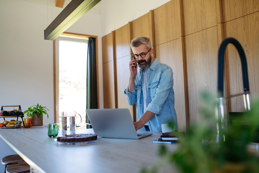 Man working from his kitchen office while on the phone, showing insurance for your home business.