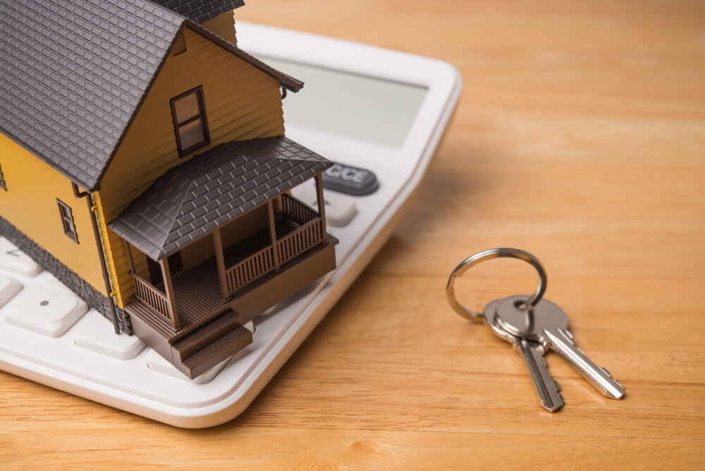 Model house on calculator with keys, symbolizing what an escrow is in managing home purchase funds.