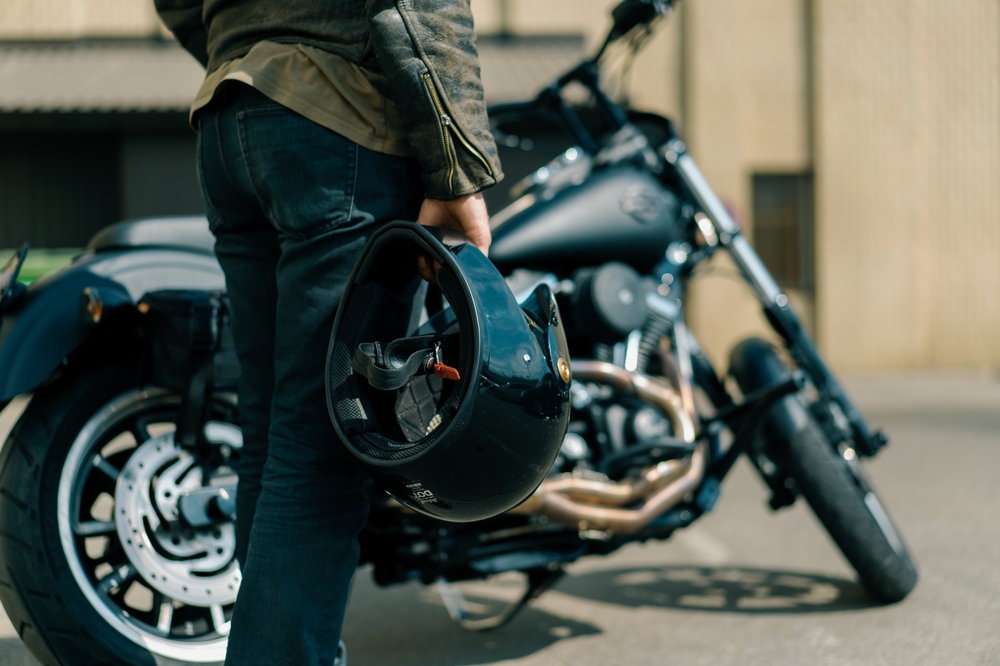 Motorcyclist holding a helmet beside a parked bike, illustrating why motorcycle insurance is mandatory for protection.
