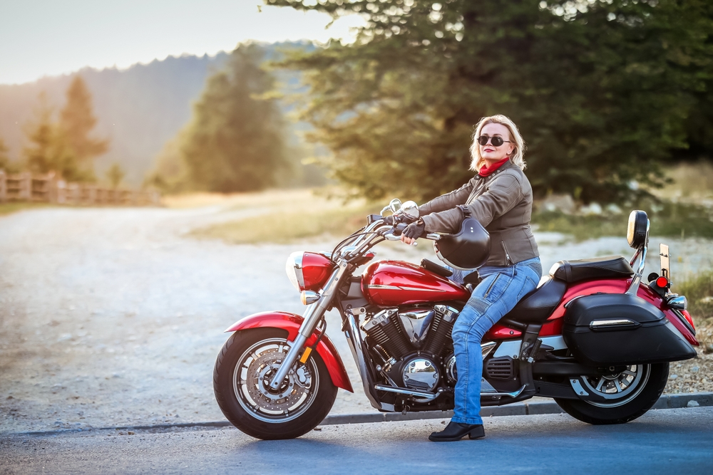 Woman sitting on a motorcycle outdoors, representing why motorcycle insurance is mandatory for riders.
