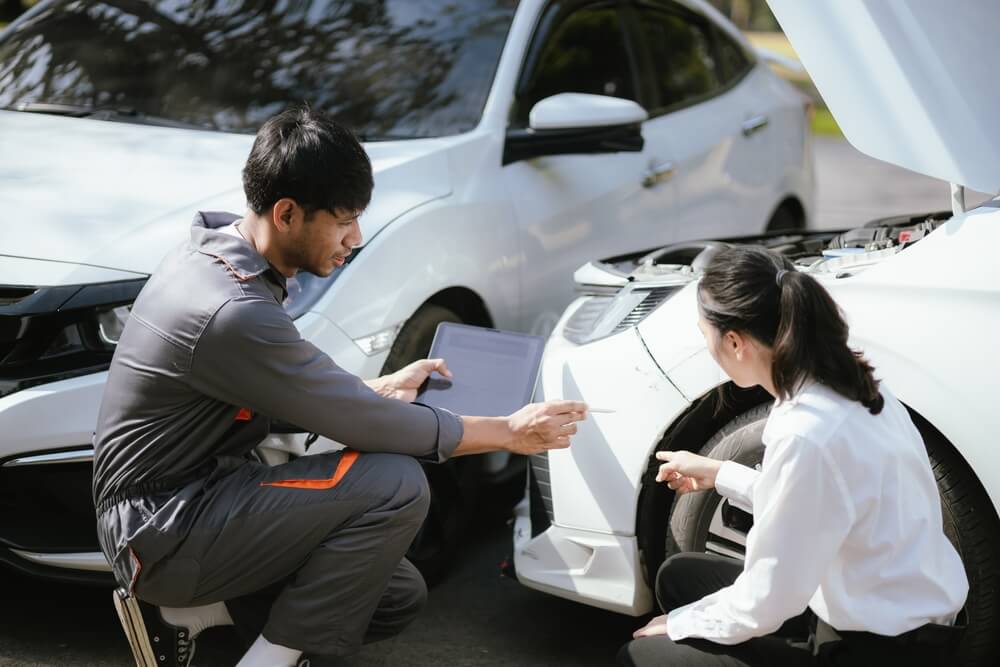 Mechanic reviewing damage with a driver beside a car, explaining repair costs and how a car insurance deductible applies before coverage pays.