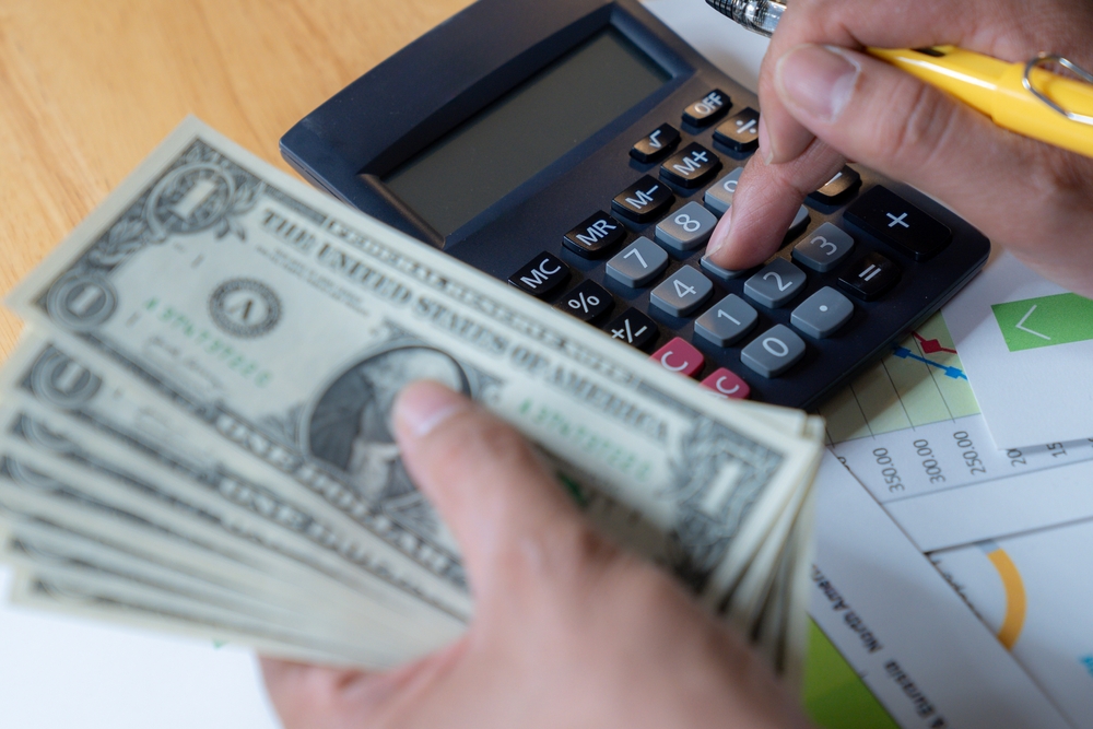 Symbolic image of a hand with a fistful of money and an adding machine