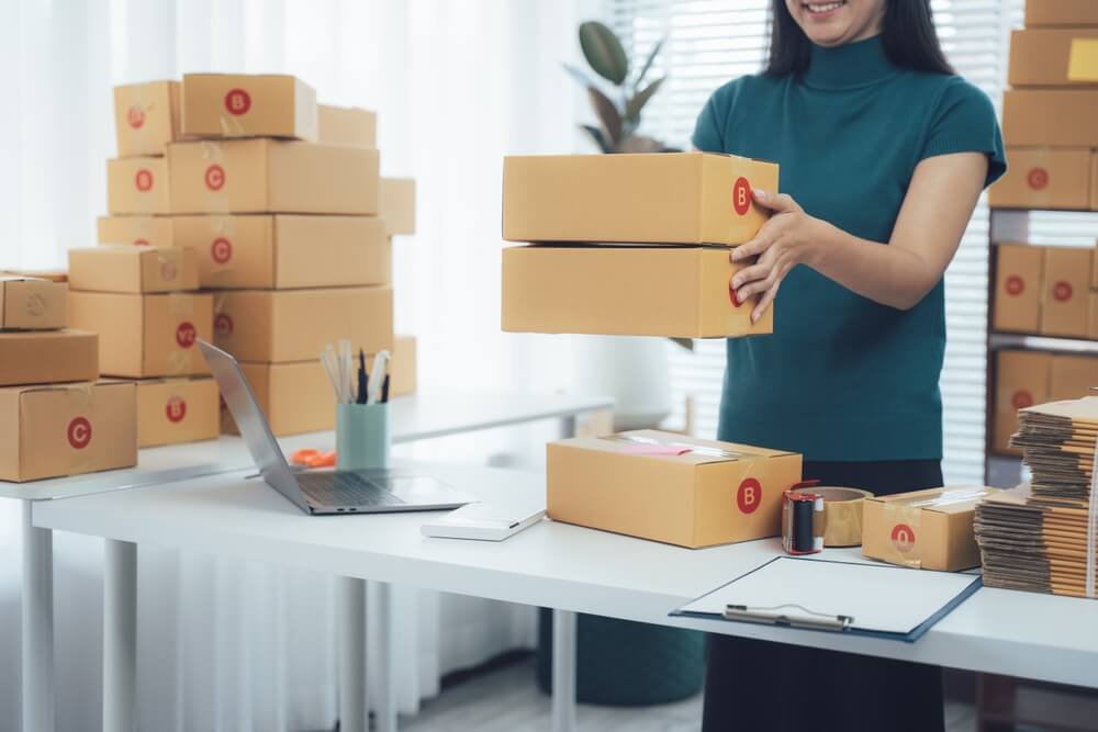 Woman packing shipping boxes for an ecommerce business, illustrating the need for online business insurance and business protection.