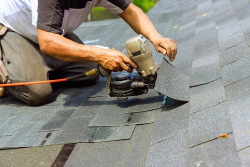 Contractor repairing a roof by installing new shingles with a nail gun