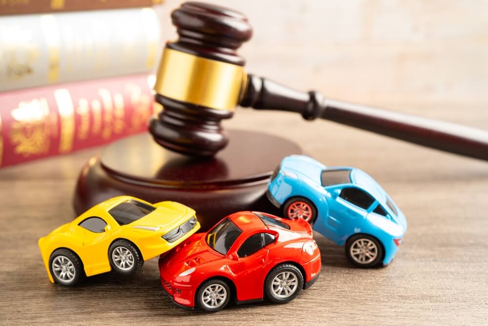 Toy cars involved in a collision beside a judge’s gavel, representing legal issues and car insurance record consequences after an accident.