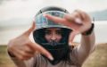 Woman wearing a full-face motorcycle helmet frames the camera with her hands, highlighting Motorcycle Helmets and Insurance.
